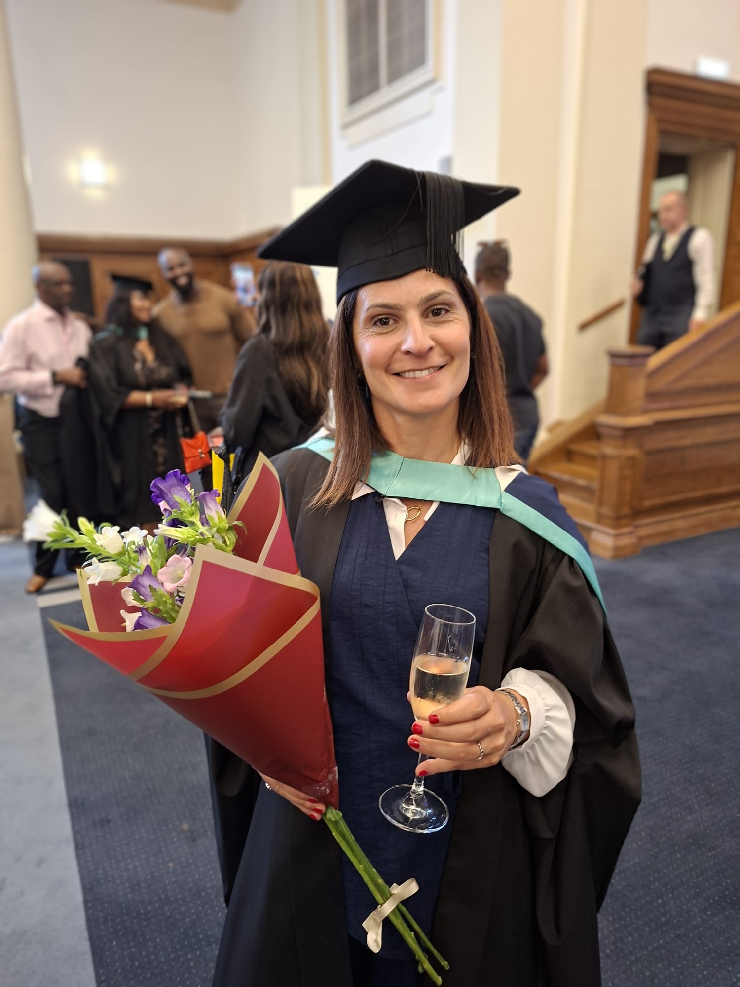 Silvia Iommi in cap and gown holding flowers and a glass of champagne after her graduation ceremony